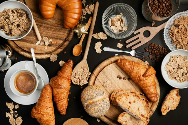 Croissants, pães e café sobre uma mesa escura.